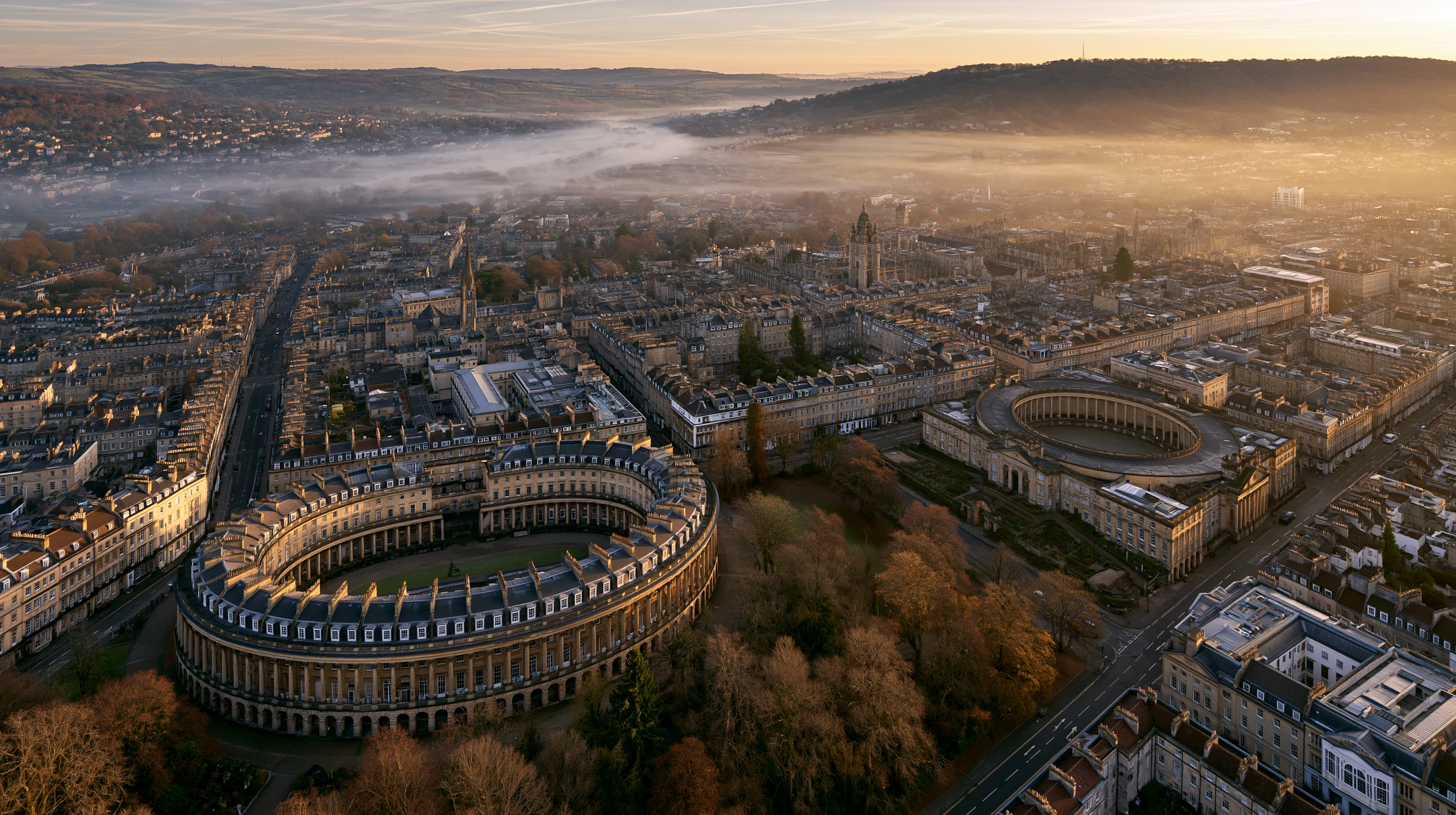 An aerial photograph of central Bath at sunrise. The Royal Crescent is visible left of centre.